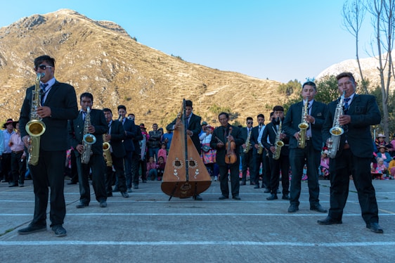 A group of musicians playing wind instruments, percussion, and guitar outdoors in a lush farm field during sunset.