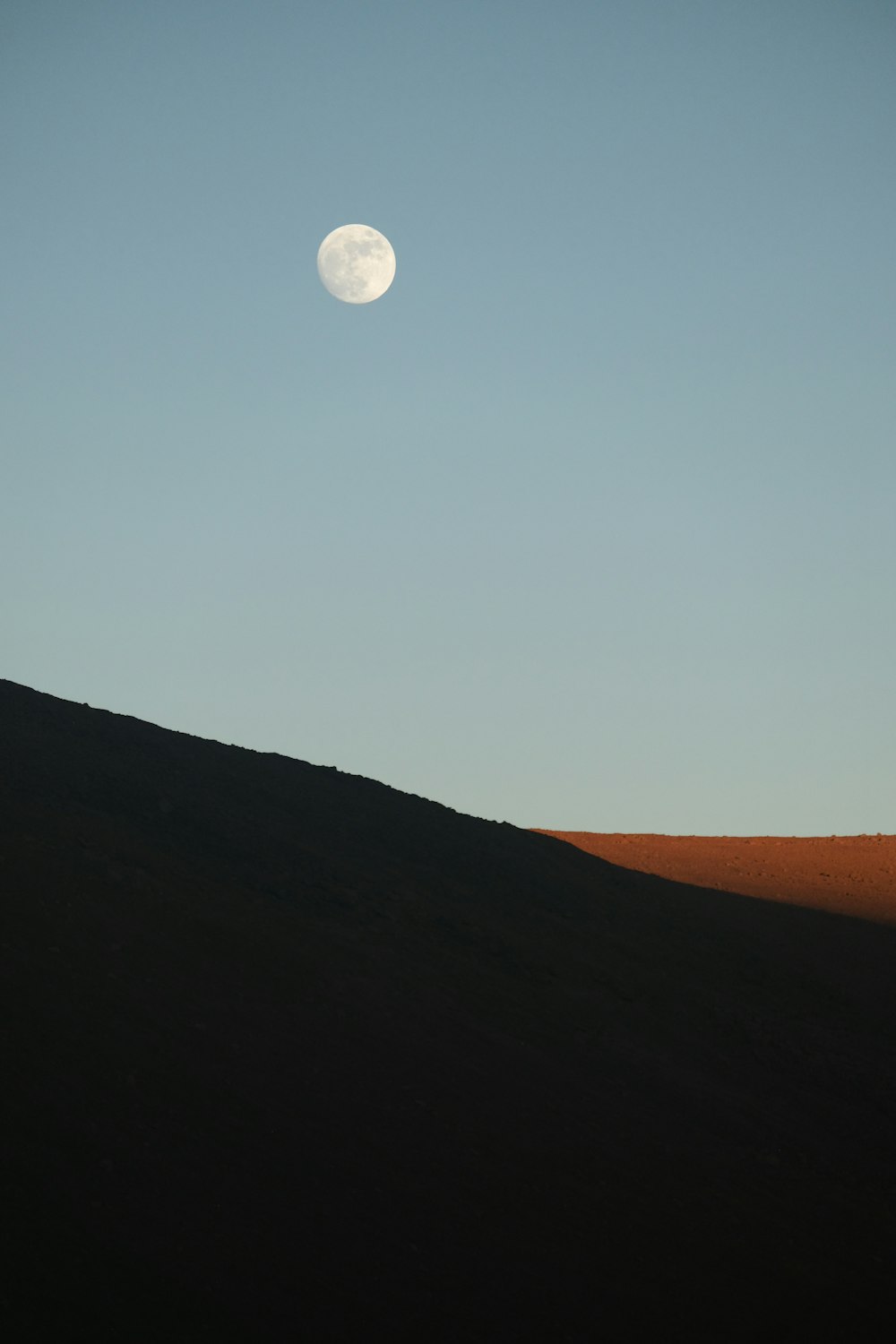 the moon is setting over a hill in the desert