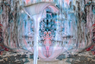 An abstract painting with fluid, swirling patterns combining blue, pink, white, and gray. The central focus is a waterfall-like structure with flowing lines and a mirrored background, creating a symmetrical, dreamlike effect.