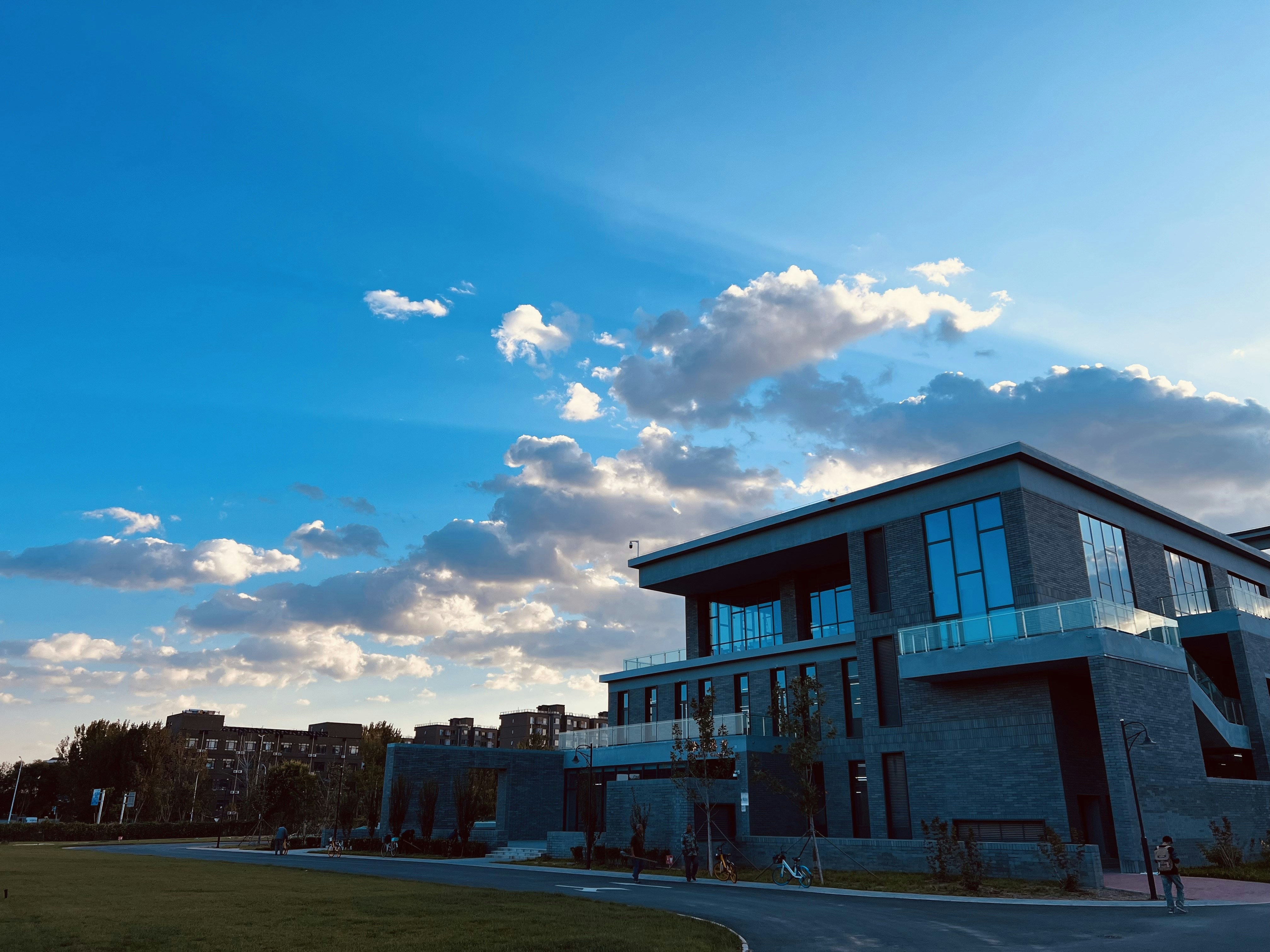 A modern academic building with students walking in front, under a clear blue sky.