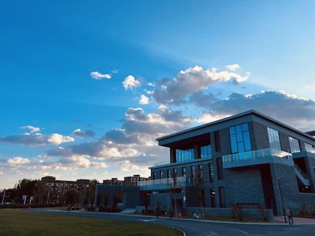A modern school building with clean lines and students engaging in outdoor learning activities under a bright blue sky.
