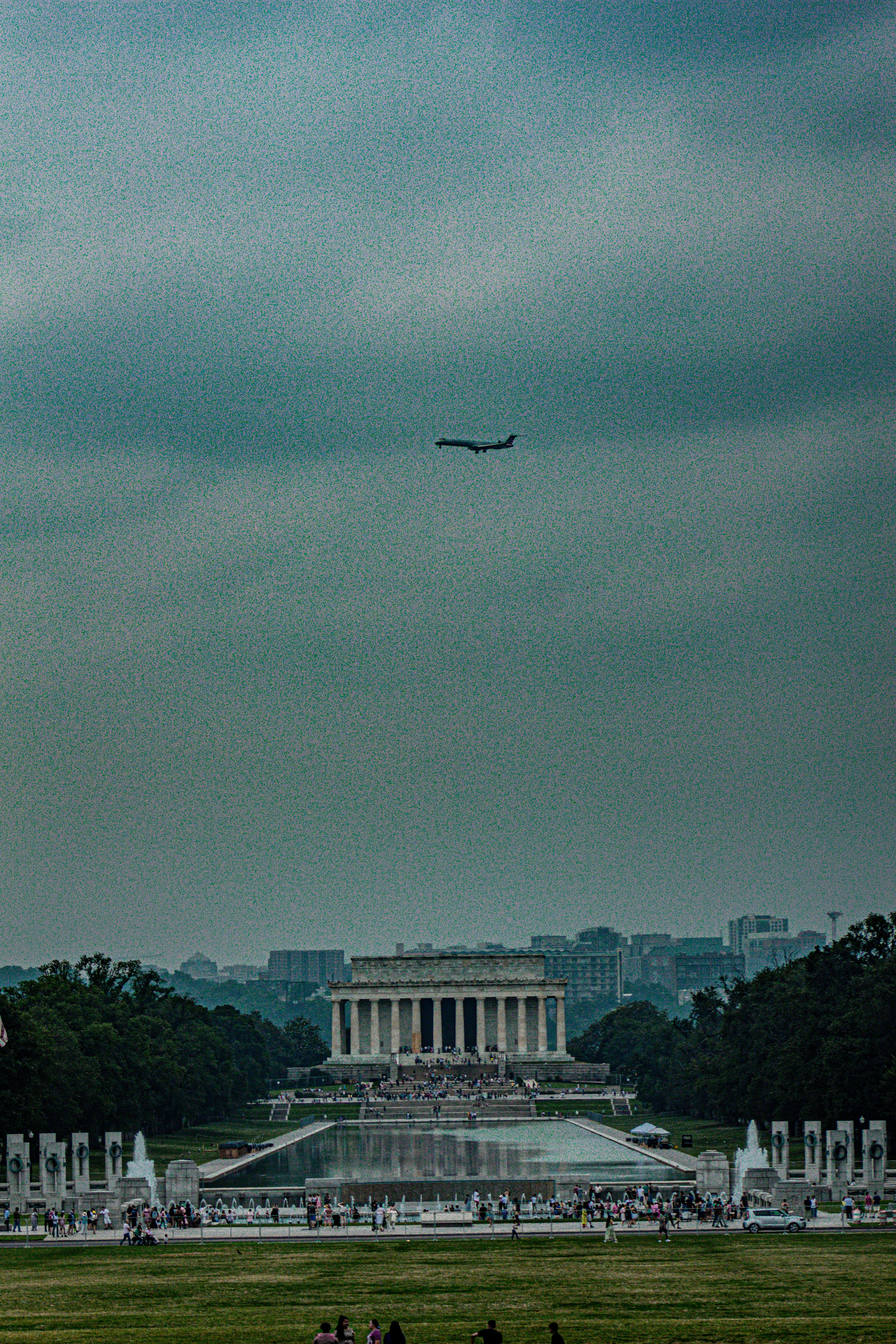 a large jetliner flying over a lush green field