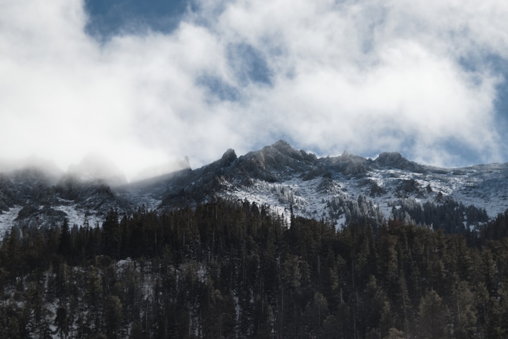 a snow covered mountain with trees and clouds