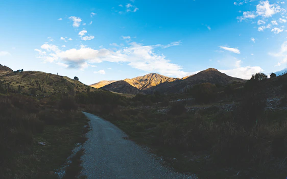A serene mountain landscape with a winding path leading toward a distant horizon under soft morning light.