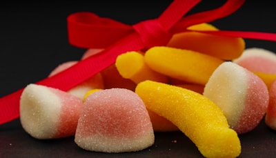 A group of sugar-coated jelly candies in pastel pink and yellow hues is tied together with a bright red ribbon, set against a dark background.