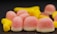 A pile of colorful gummy candies, including pink and white dome-shaped ones and elongated yellow ones, covered in a sugary coating, set against a dark background.