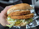 Close-up of hands exchanging a wrapped sandwich through a car window at night with subtle smoke in the background.