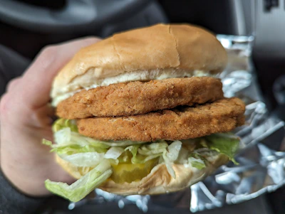 Close-up of hands exchanging a wrapped sandwich through a car window at night with subtle smoke in the background.