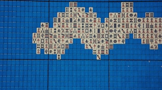 A mosaic pattern composed of Mahjong tiles is arranged on a grid of vibrant blue square tiles. The Mahjong tiles feature various traditional Chinese characters and symbols in red and black inks.