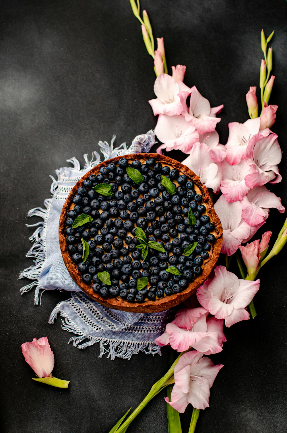 a bowl of blueberries and pink flowers on a table