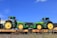 Two green tractors with large yellow wheels are placed on flatbed train cars. The tractors appear new and display branding. The sky is clear and blue in the background.