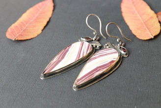 Elegant pair of silver earrings with subtle pink accents displayed on a white marble surface.