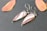 A pair of teardrop-shaped earrings with a marbled pattern of pink and white inside a silver setting are placed on a textured, dark gray surface. Two autumn-colored leaves lie beside them, adding a warm contrast.