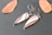 A pair of teardrop-shaped earrings with a marbled pattern of pink and white inside a silver setting are placed on a textured, dark gray surface. Two autumn-colored leaves lie beside them, adding a warm contrast.