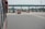 A highway toll plaza featuring several lanes for vehicles to pass through. Red and white traffic cones and barriers are placed around the lanes, and vehicles, including buses and trucks, are waiting to move forward. There is a sign with text on the structure overhead.