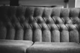 A close-up of a dark, tufted sofa backrest with soft, cushioned buttons arranged in a diamond pattern.