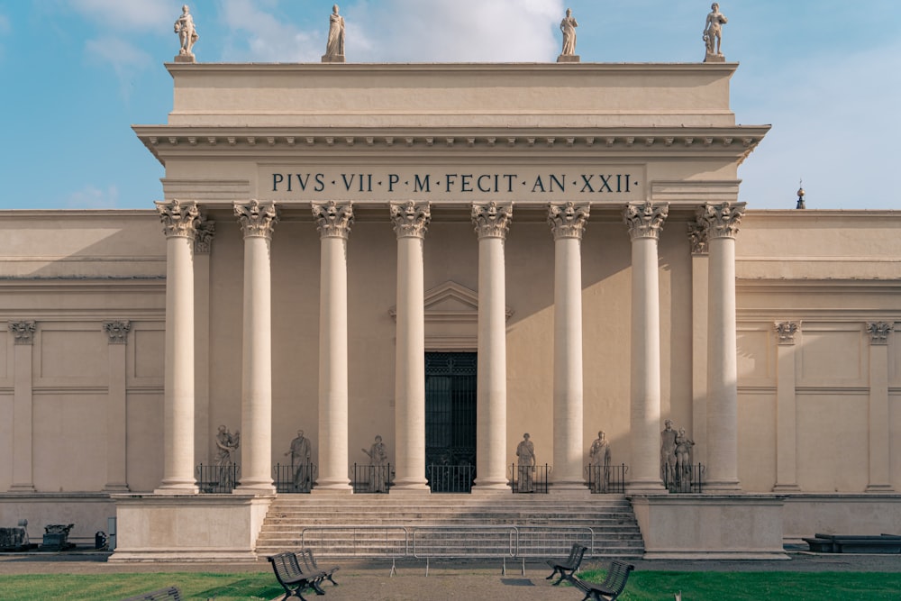 the front of a building with columns and benches in front of it