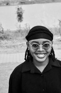 Person wearing stylish round sunglasses smiling outdoors with greenery behind
