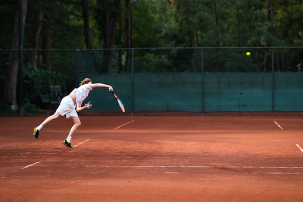 A tennis coach demonstrating a training technique to a focused student on the court.