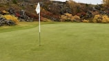 Crowd cheering by the final hole with colorful fall foliage in the background.
