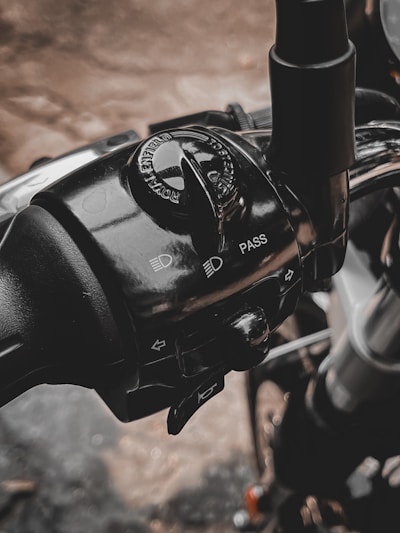 A detailed view of a motorcycle control panel, featuring switches and controls for headlights and pass signals. The branding of a motorcycle company is visible on the rotary switch. The metallic and plastic components are highlighted with reflections and shadows.