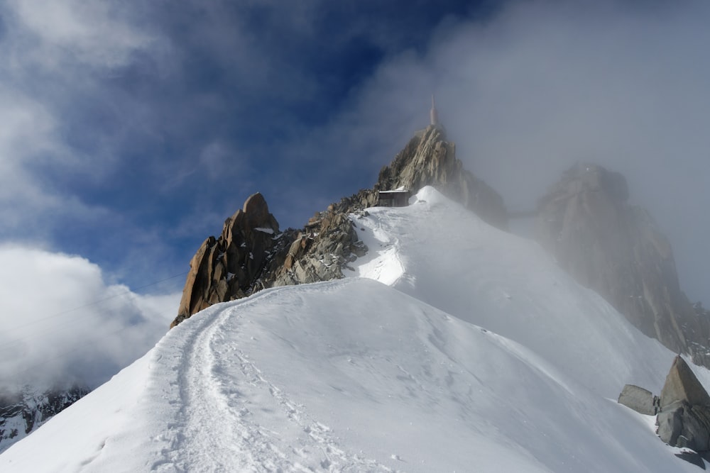 a mountain covered in snow and clouds under a blue sky