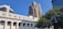 A classical courthouse building with columns is in the foreground, with modern high-rise buildings rising behind it under a clear blue sky. A large, leafy tree is present on the right side of the image, adding a natural element to the urban setting.