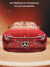 A sleek, futuristic red car is prominently displayed with a shiny and modern design. The car features a distinctive logo on the front grille and is set against a stylish background with warm, orange lighting. The words 'Neue Möglichkeiten der Personalisierung' and 'New level of personalization' are visible above the car, emphasizing a theme of innovation and customization.