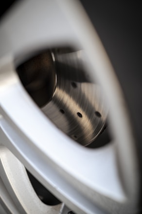 A close-up view of a sleek metallic car wheel rim focusing on the polished and shiny surface. The image highlights the curved design and precision-engineered holes, capturing the texture and sheen of the metal.