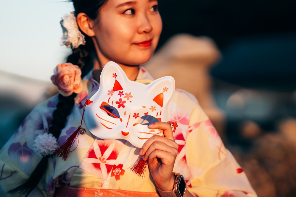 uma mulher em um quimono segurando uma máscara de gato