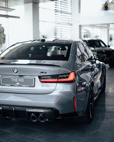 Close-up of a sleek BMW M4 with glossy black paint and electric blue accents under showroom lights.