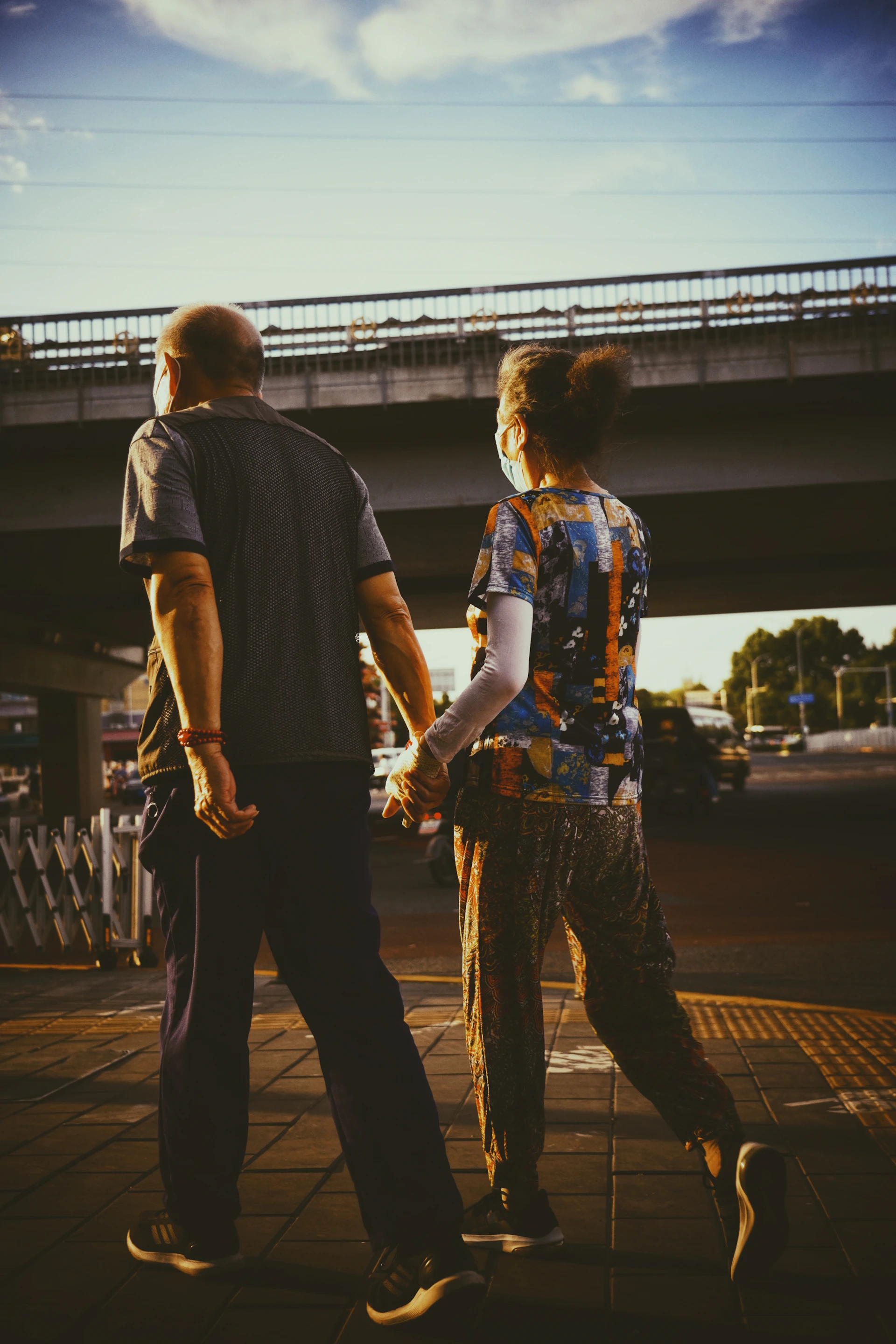 A cinematic shot of a couple walking hand-in-hand along a charcoal-colored urban street bathed in late afternoon light.