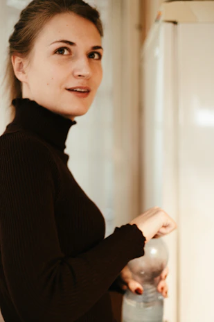 Smiling woman holding a bottle of Verdavita milk in a sunlit kitchen.