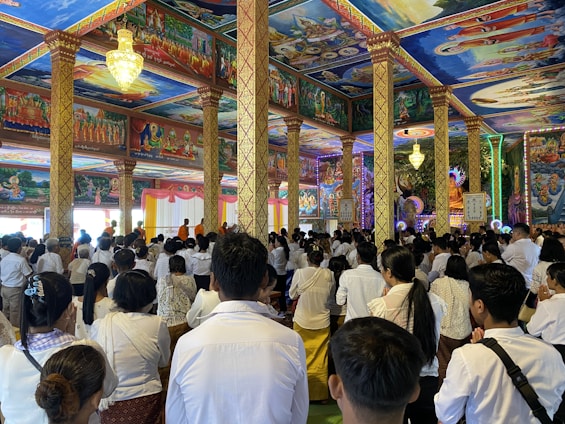A serene community hall adorned with orange, white, and golden decorations, where monks and followers meditate together.