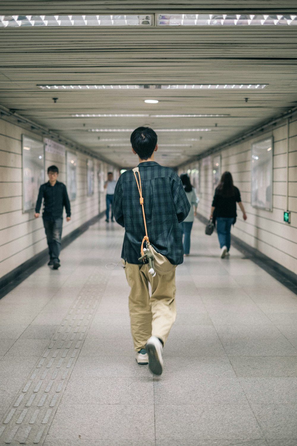 a man walking down a long hallway carrying a handbag