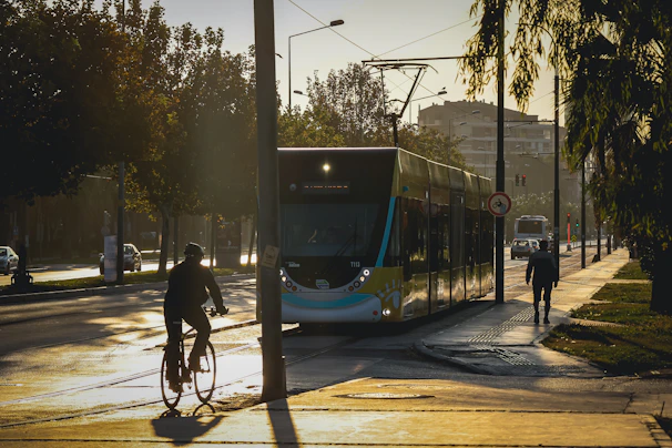 A cyclist riding a sleek e-bike through an urban street lined with trees in early morning light.