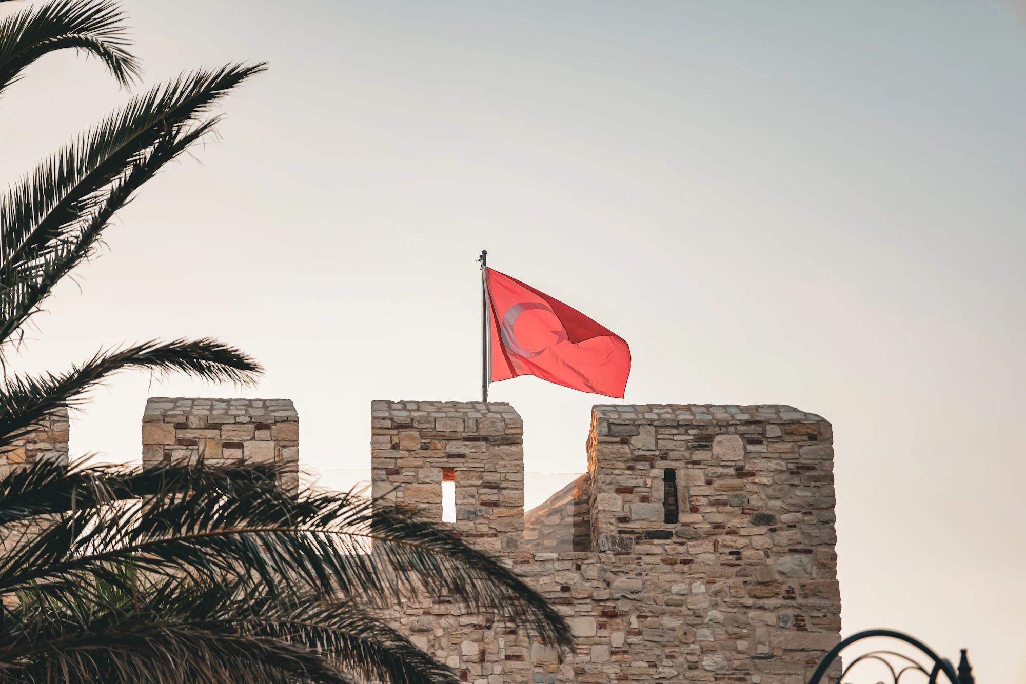 Turkish flag waving over a castle wall, symbolizing ikamet.com's expertise in Turkish immigration and residency laws.