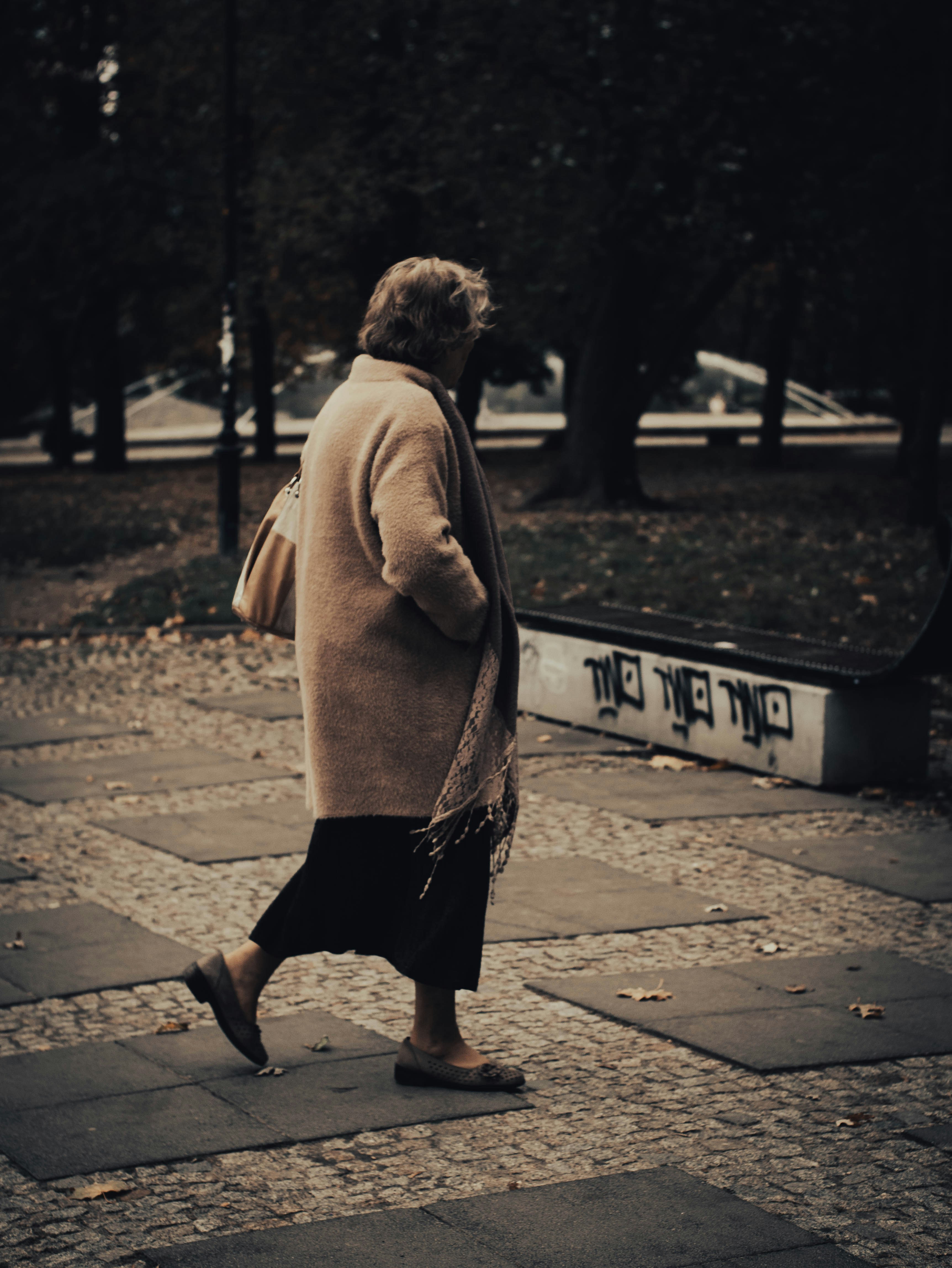 a woman walking down a sidewalk in a park