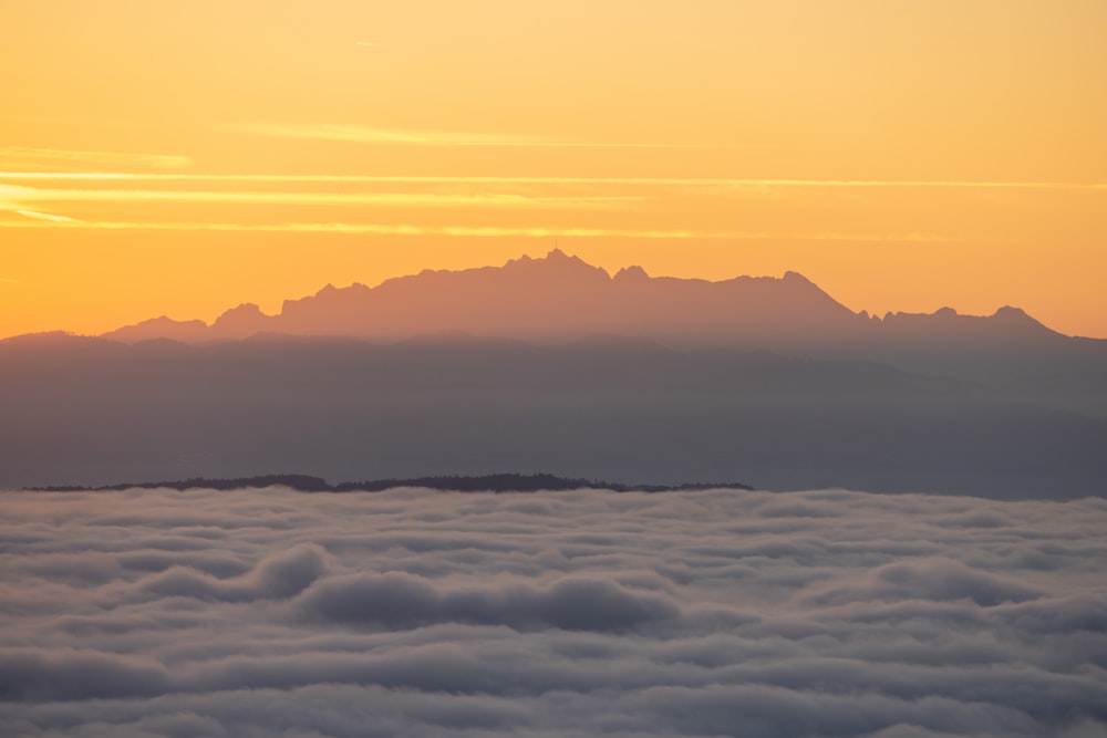 the sun is setting over the mountains above the clouds