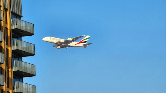 A sleek airplane taking off against a clear blue sky with Dubai's skyline in the background.