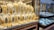 A showcase displaying a collection of intricate gold jewelry, including necklaces, earrings, bracelets, and rings, arranged on white busts and stands. The gold jewelry is highly ornate and detailed, with different designs and patterns. In the background, additional jewelry pieces are visible in a separate section behind glass.
