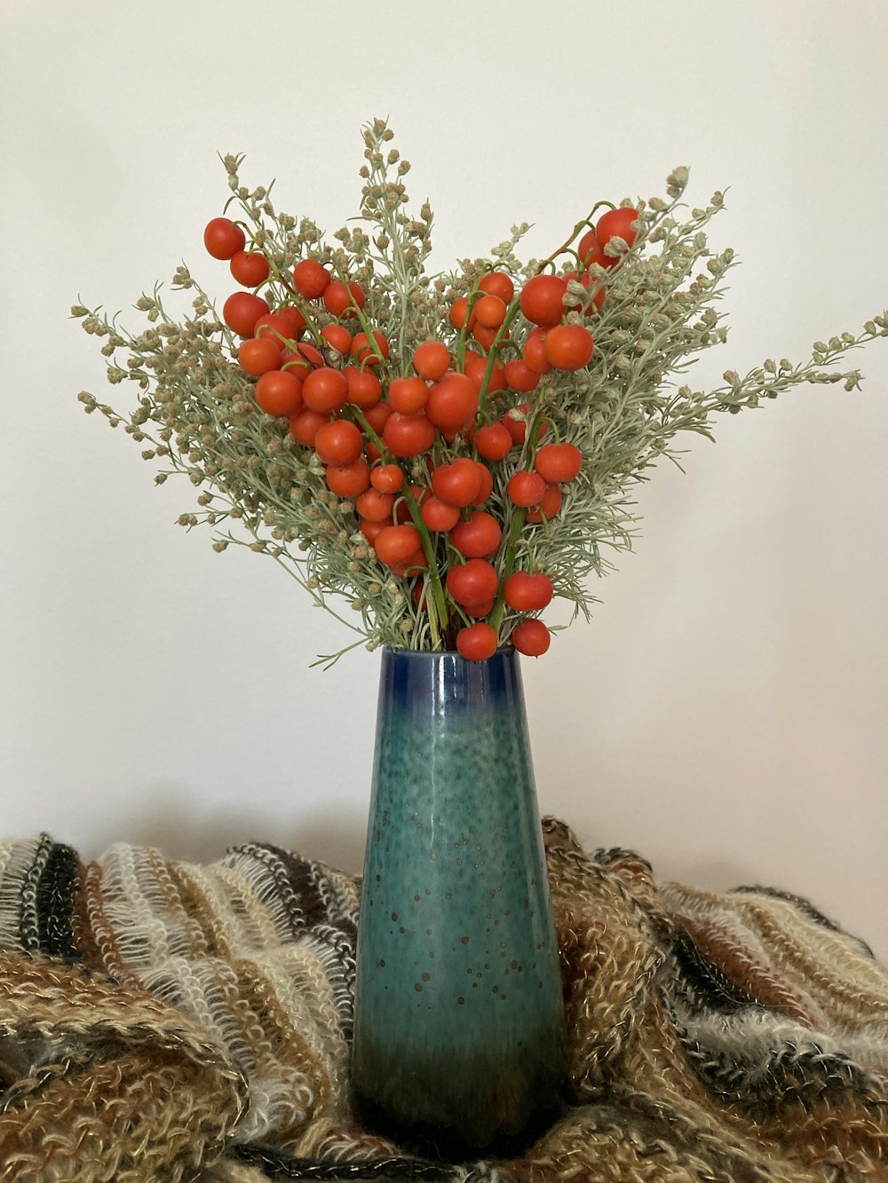 a blue vase filled with lots of red berries