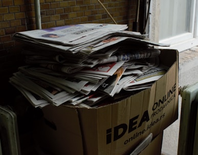 a cardboard box filled with newspapers next to a radiator