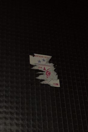 A partially peeled sticker is stuck on a dark tiled surface. The sticker has blue and red stars and some incomplete text visible.