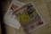 A newspaper is placed on a tiled floor. The headline in large yellow letters stands out. Next to it, there is an advertisement showing electronic massage devices. The overall setting seems casual and informal.