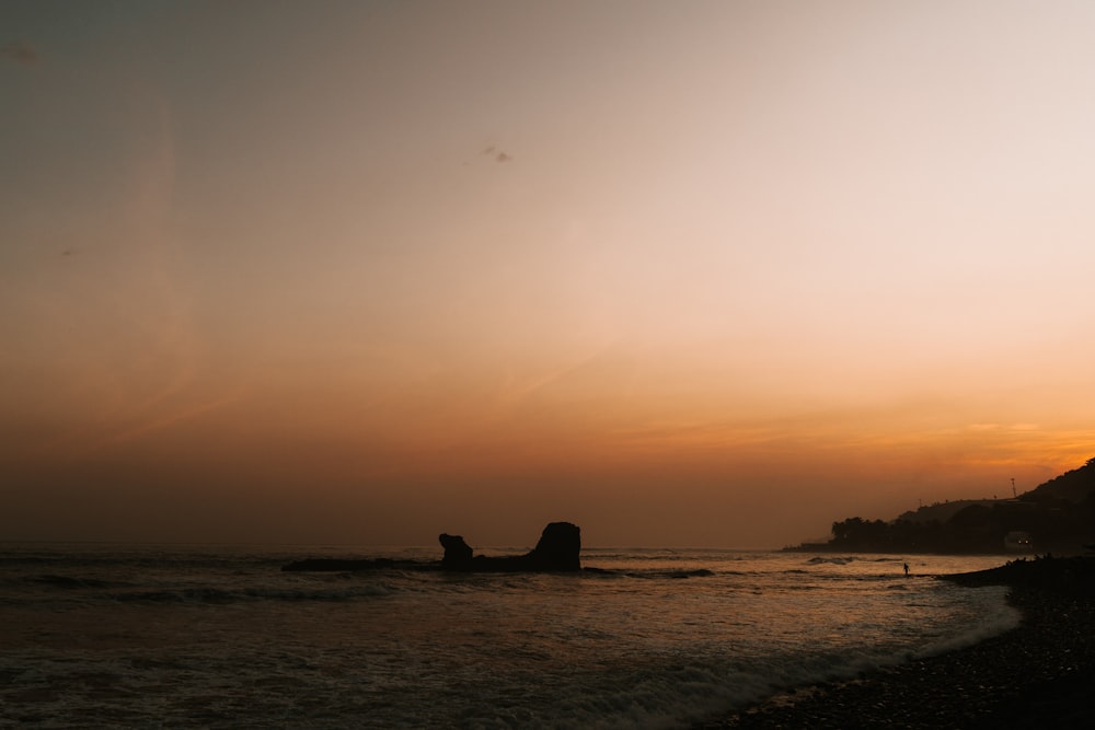 the sun is setting over the ocean with a rock outcropping