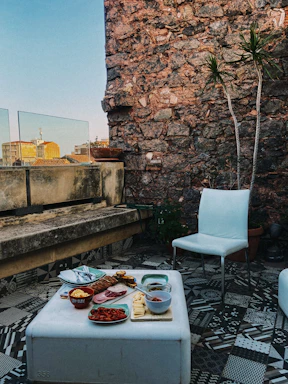 A cozy terrace setting by the sea featuring a beautifully arranged plate of crispy patatas bravas with a side of rustic bread and a small bowl of pink aioli.