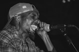 A person wearing a patterned shirt and a backwards cap is passionately singing into a microphone, conveying intense emotion and energy.