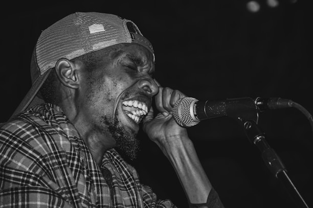 A person wearing a patterned shirt and a backwards cap is passionately singing into a microphone, conveying intense emotion and energy.