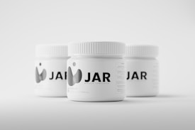 Three white jars with ribbed lids are arranged on a light background. The jars are labeled with the text 'JAR' accompanied by a minimalist graphic logo. They appear to be mockup templates for product design presentation.